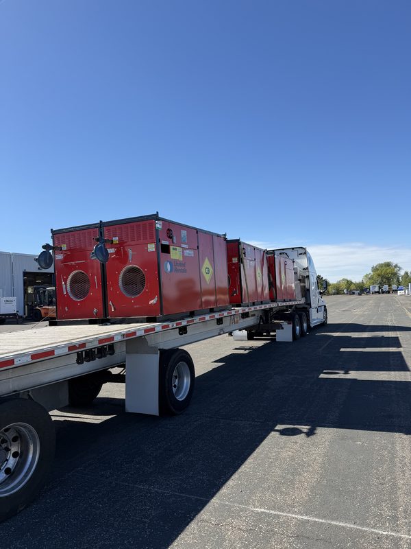 Flatbed loaded with red industrial heater units behind a white semi truck
