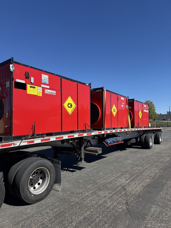 Close side view of red heater units chained and strapped on a flatbed trailer