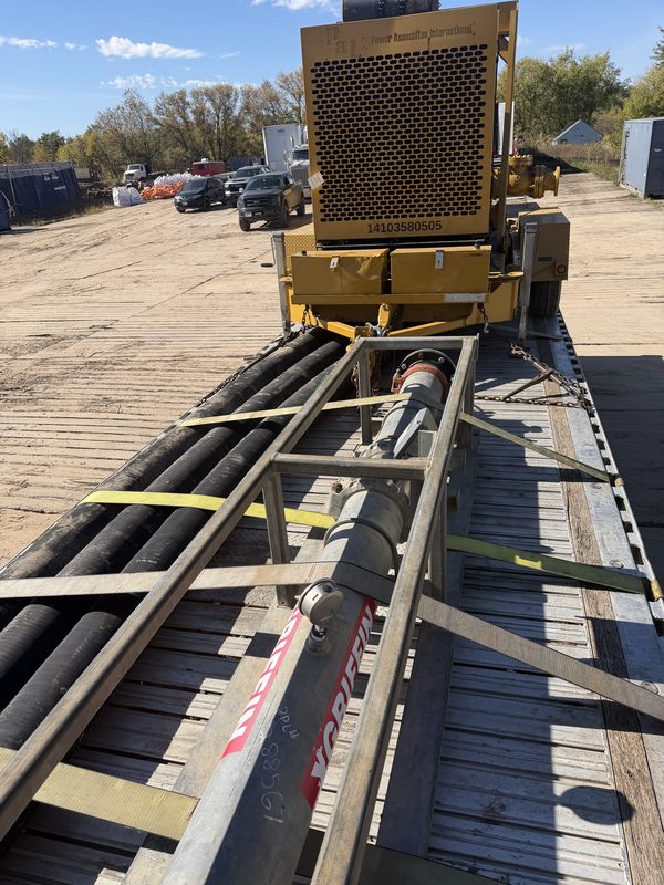 Large black hoses and steel pipe strapped down with yellow straps on a flatbed