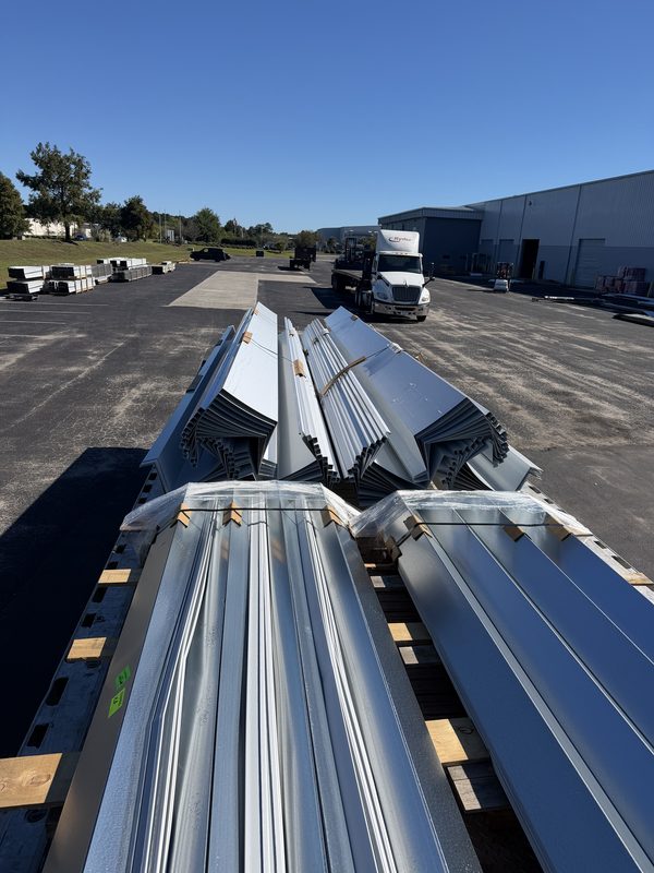 Flatbed loaded with bundles of roofing metal panels on wood dunnage at a warehouse yard